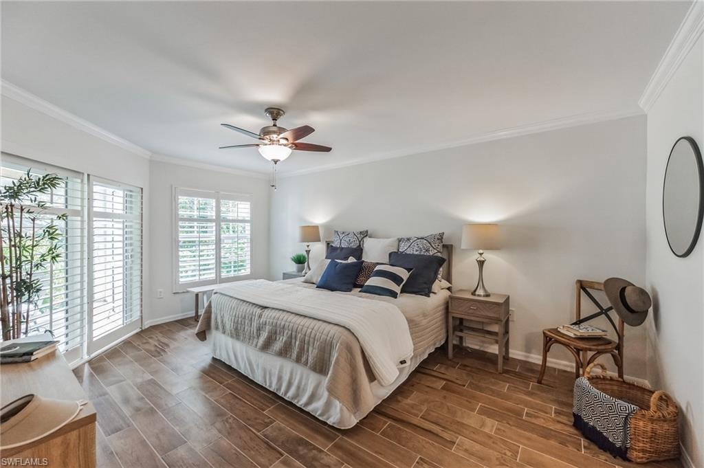Bright bedroom featuring wood-finish flooring, white plantation shutters, a ceiling fan with integrated lighting, and crown molding