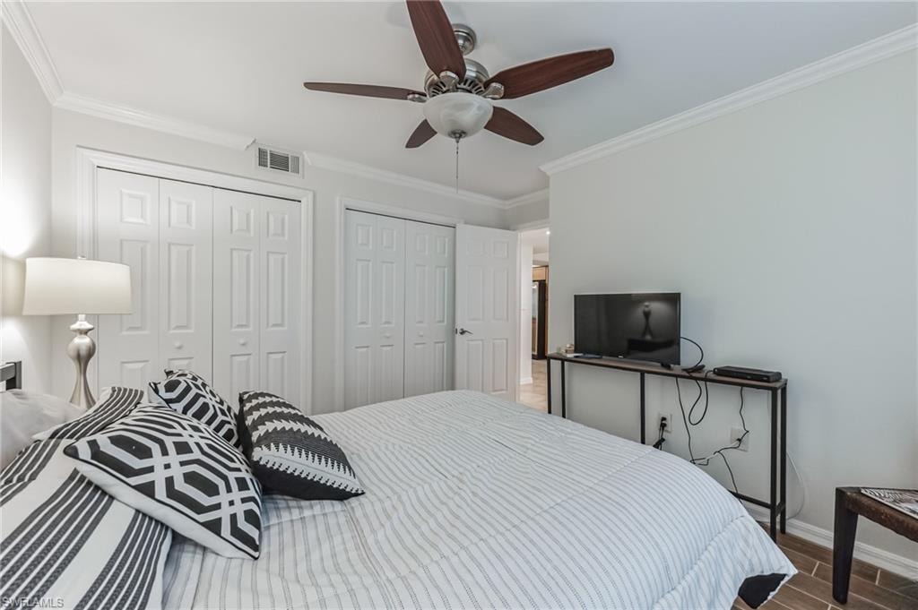 Bedroom featuring a ceiling fan with wood-finish blades, crown molding, white bi-fold closet doors, and wood-look flooring