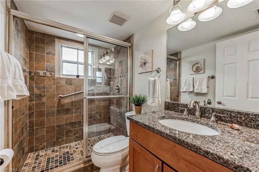 Full bathroom featuring a granite countertop vanity with an undermount sink, a tiled walk-in shower with mosaic flooring, and a glass shower enclosure