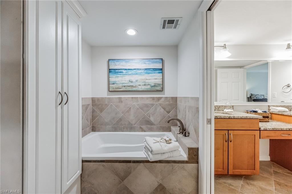 Built-in soaking tub with a tiled surround, recessed lighting, and integrated storage cabinetry