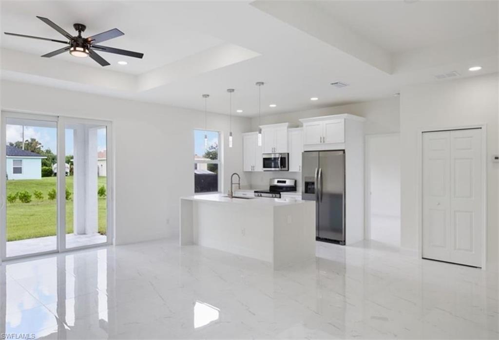 Open-concept living space with sleek tile flooring, a modern kitchen island, white cabinetry, and stainless steel appliances