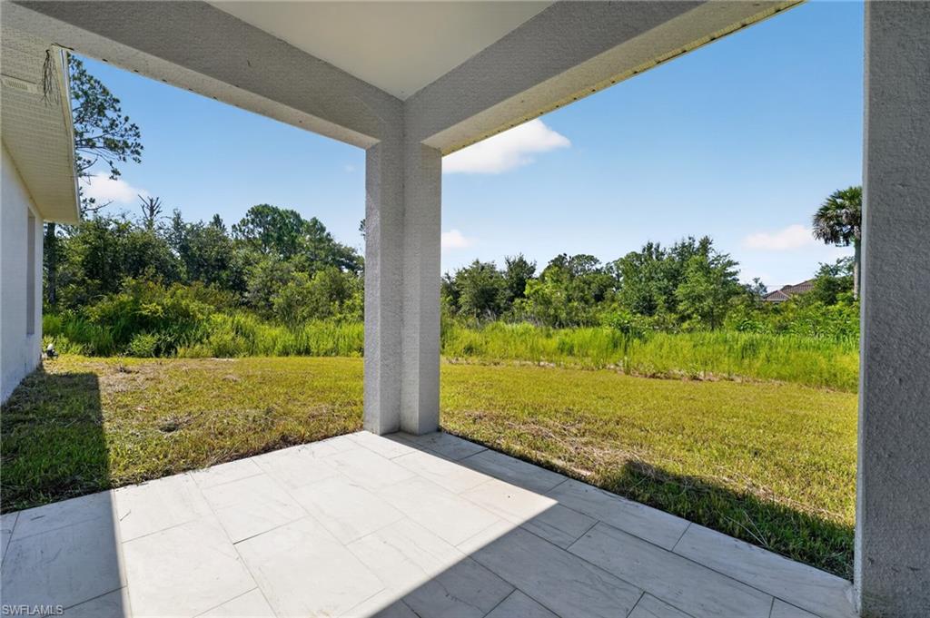 Covered patio with tile flooring and stucco columns, overlooking a spacious green area with natural landscaping
