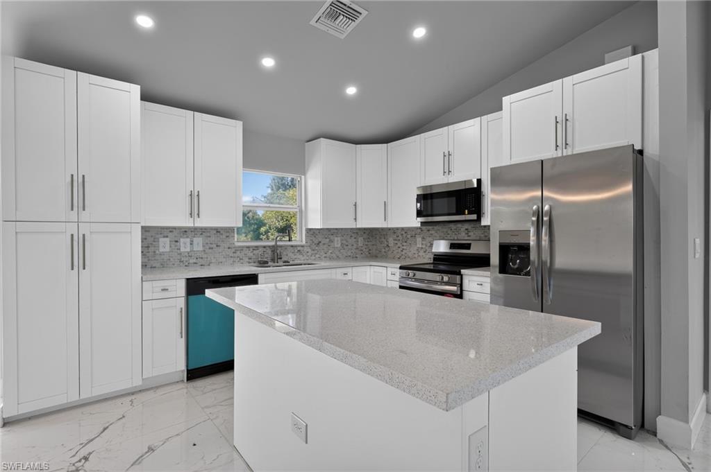 Contemporary kitchen featuring white cabinetry, a large center island with a light-toned countertop, a stainless steel side-by-side refrigerator, a matching microwave, and a mosaic tile backsplash
