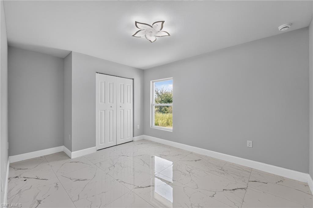 Bright room featuring large format tile flooring, a window with outdoor scenery, closet with bi-fold doors, white baseboards, and a decorative ceiling light fixture