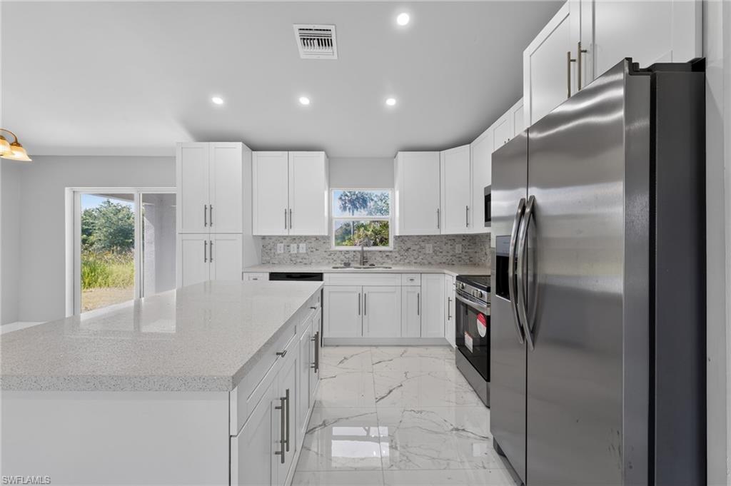 Modern kitchen featuring white shaker cabinetry, stainless steel appliances, a spacious island with a light-toned countertop, and white tile flooring