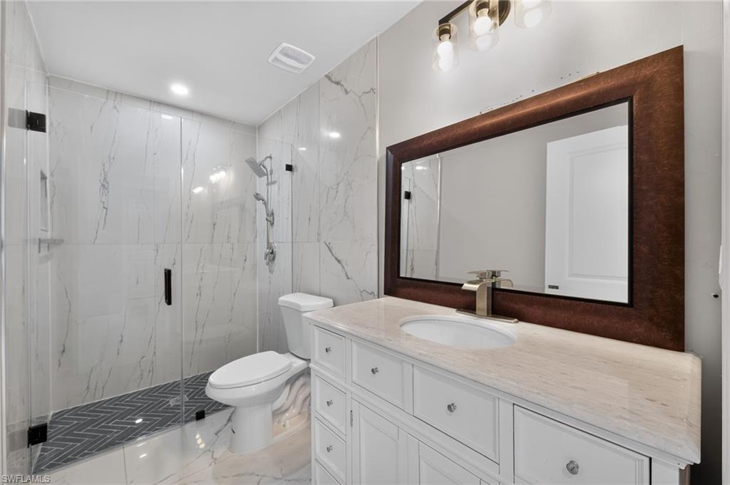 Contemporary bathroom featuring a spacious glass-enclosed shower with herringbone tile flooring, a white vanity with extensive drawer storage, a light-toned countertop, and a large framed mirror with overhead lighting