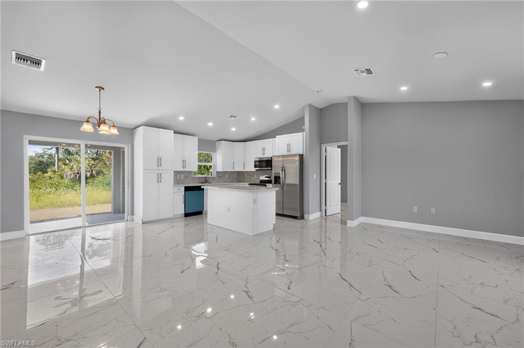 Open-concept living space featuring high ceilings, large format tile flooring, a modern kitchen with white cabinetry and stainless steel appliances, and sliding glass doors leading to the outdoors