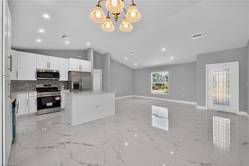 Open-concept living area featuring a kitchen with white cabinetry, stainless steel appliances, and a central island