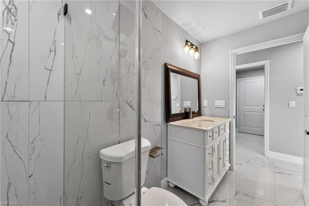 Bathroom featuring large format marble-look tile walls and flooring, a white vanity with a light-colored countertop and integrated sink, a framed mirror, and a three-bulb vanity light fixture