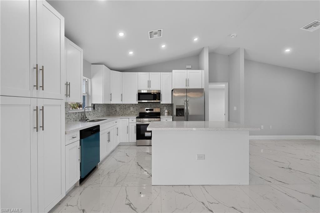 Modern kitchen featuring white shaker cabinetry, stainless steel appliances, a white island, light-toned countertops, and a mosaic tile backsplash