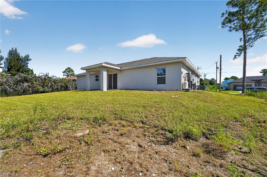 Expansive rear yard featuring a covered patio, multiple exterior windows, and mature perimeter landscaping