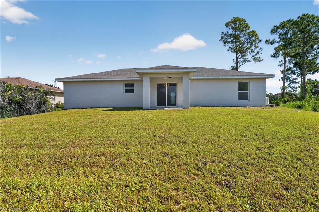 Expansive rear yard featuring green lawn, concrete block construction, and sliding glass doors