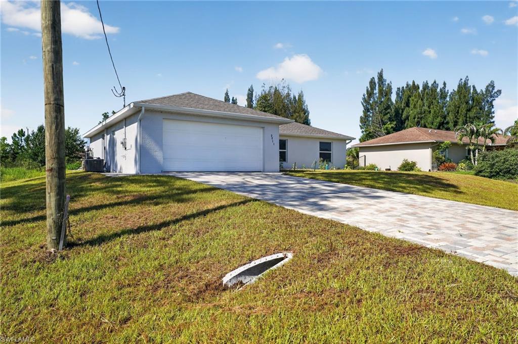 Single-story residence featuring a two-car garage, light-toned exterior siding, and a patterned paver driveway