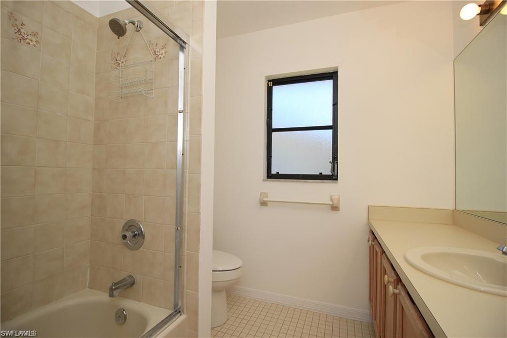 Full bathroom with tile floors, shower / bath combination with glass door, large vanity, and toilet