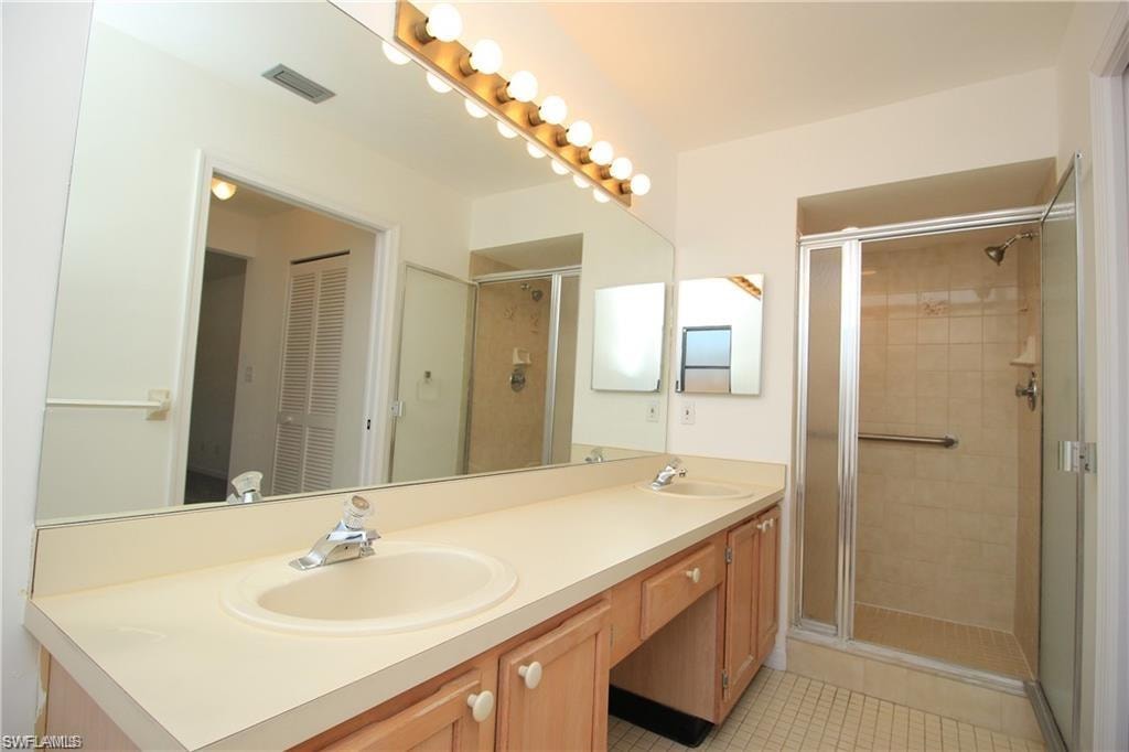 Bathroom featuring a shower with door, tile floors, large vanity, and double sink