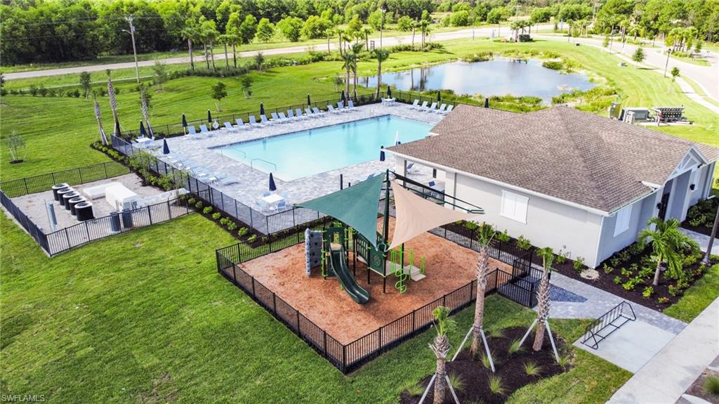 Community recreation area featuring a large swimming pool, paved sundeck with lounge chairs, playground with shade sails, and an adjacent structure with a covered entry