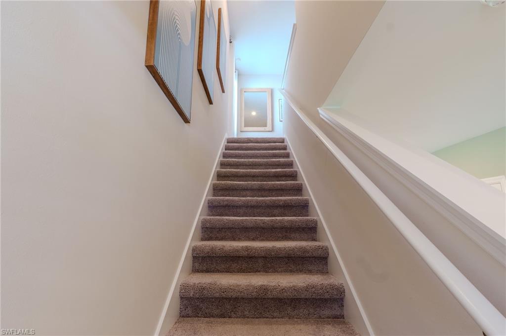 Carpeted staircase with white handrail and trim, leading to an upper level with light-colored walls