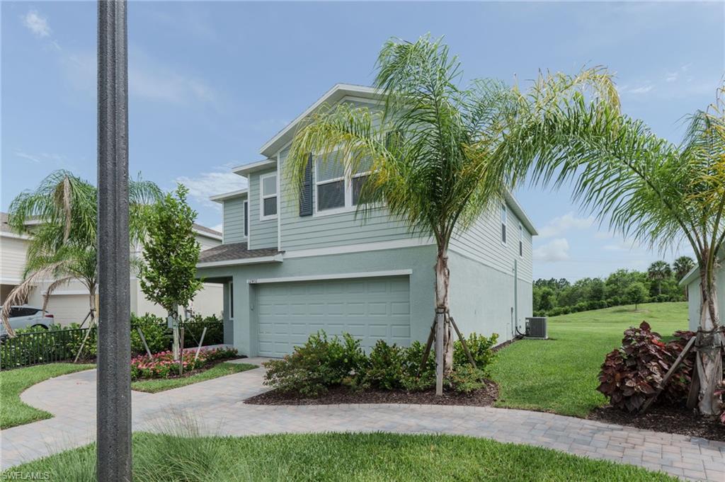 Contemporary two-story exterior featuring a light green and gray facade, an integrated garage, a paver driveway, mature palm trees, and lush landscaping