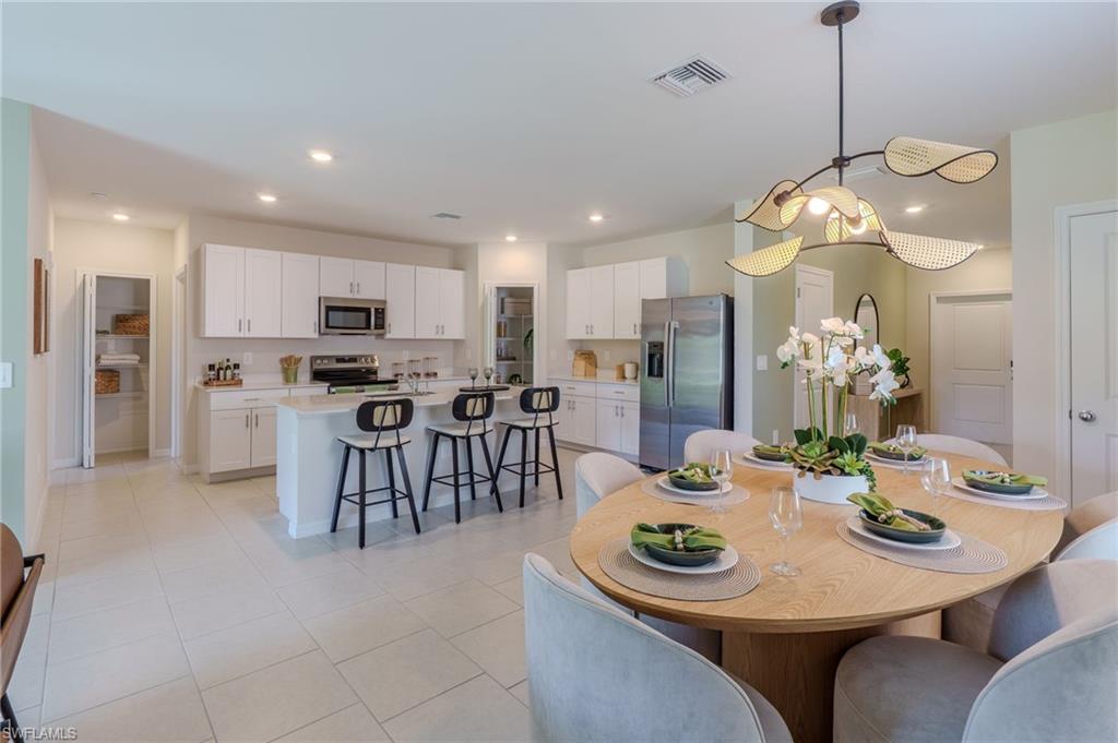 Open-concept kitchen and dining area featuring a kitchen island with seating, stainless steel appliances, white cabinetry, and recessed lighting