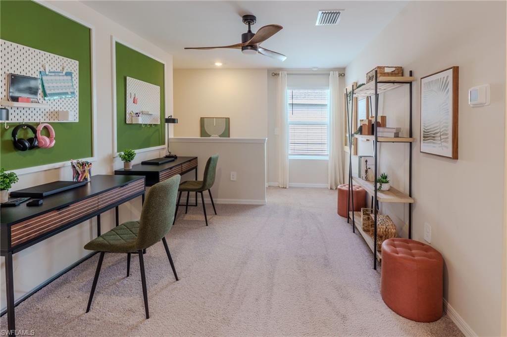 Carpeted loft space featuring dual desk areas with green accent walls, a ceiling fan, and a window with blinds