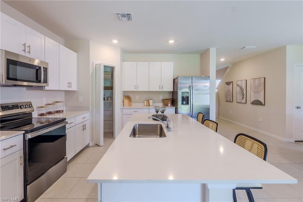 Open-concept kitchen featuring white cabinetry, stainless steel appliances, a large center island with an undermount sink, and light-toned tile flooring