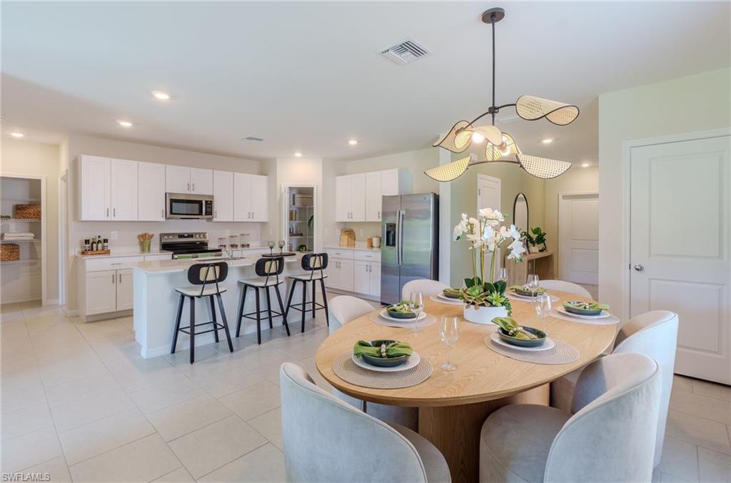 Open-concept kitchen and dining area featuring white cabinetry, stainless steel appliances, a kitchen island with seating, and light-toned tile flooring