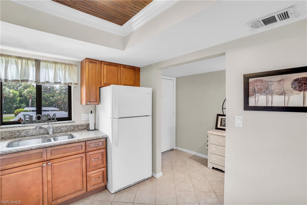 Kitchen featuring sink, white fridge, light tile patterned floors, and light stone counters