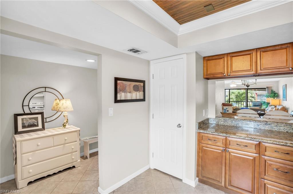 Kitchen with light tile patterned flooring, wood ceiling, light stone counters, and crown molding
