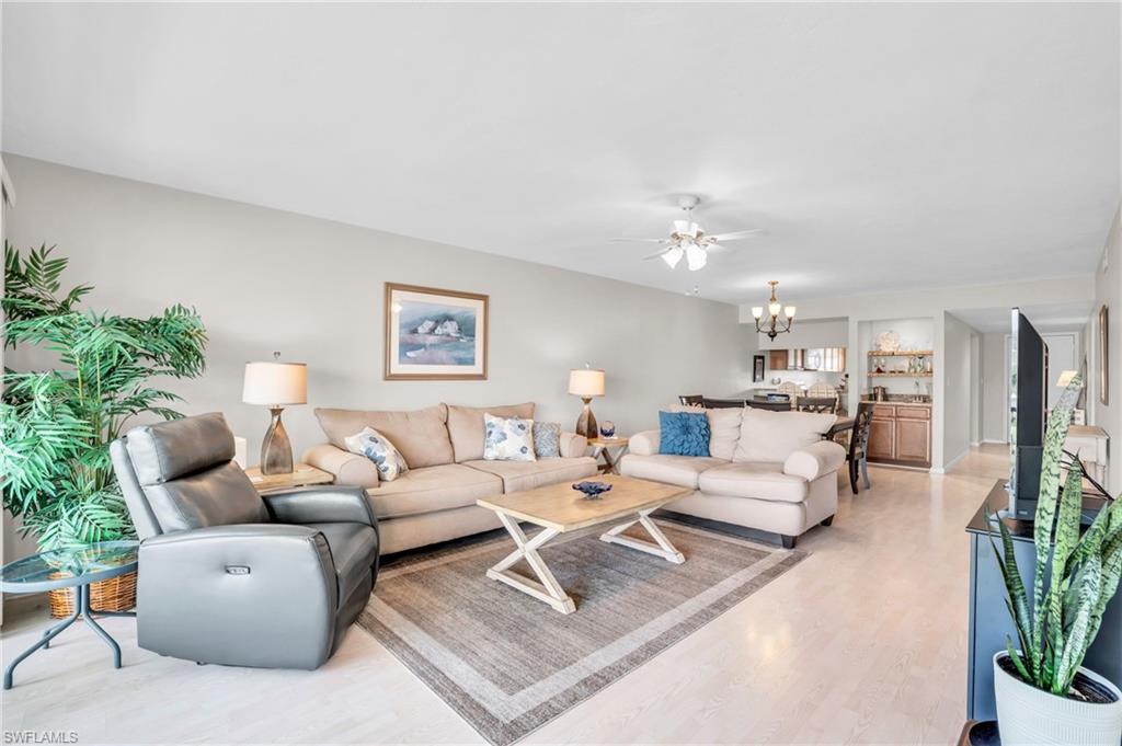 Living room with ceiling fan with notable chandelier and light hardwood / wood-style floors