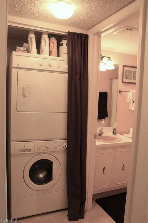 Washroom with a textured ceiling and stacked washing machine and dryer