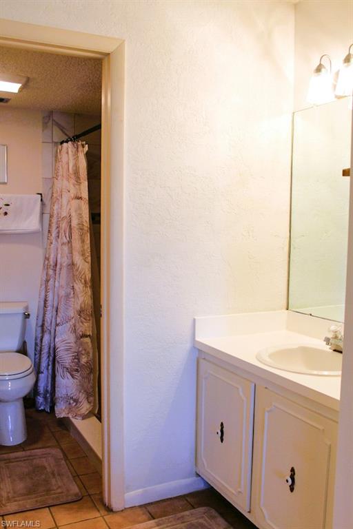 Full bathroom featuring a stall shower, vanity, a textured ceiling, a textured wall, and dark tile patterned floors