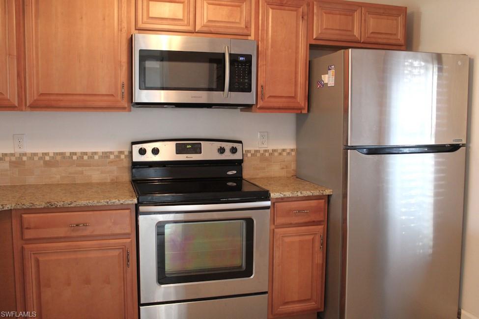 Kitchen with appliances with stainless steel finishes, light stone countertops, and brown cabinets