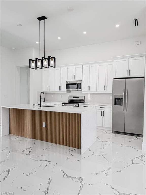 Gourmet kitchen featuring a central island with wood paneling, white countertops, and a contemporary black pendant light fixture