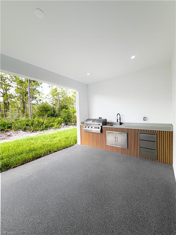 Covered outdoor kitchen featuring a built-in grill, integrated sink with a black faucet, and stainless steel cabinetry