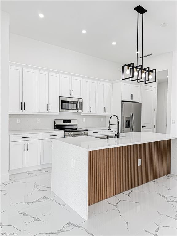 Modern kitchen featuring white shaker cabinetry, stainless steel appliances, and a central island with a wood-slat accent and white countertop