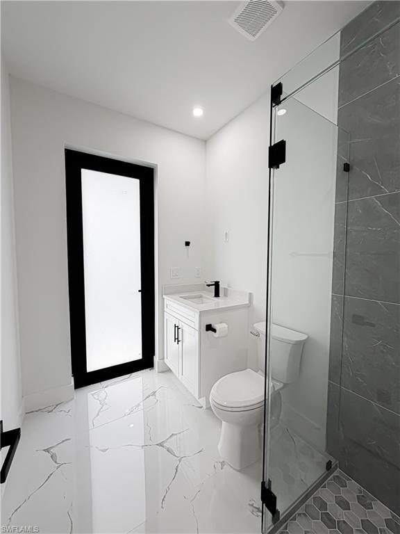 Modern bathroom featuring white walls, large format white tile flooring with gray veining, and a clear glass shower enclosure