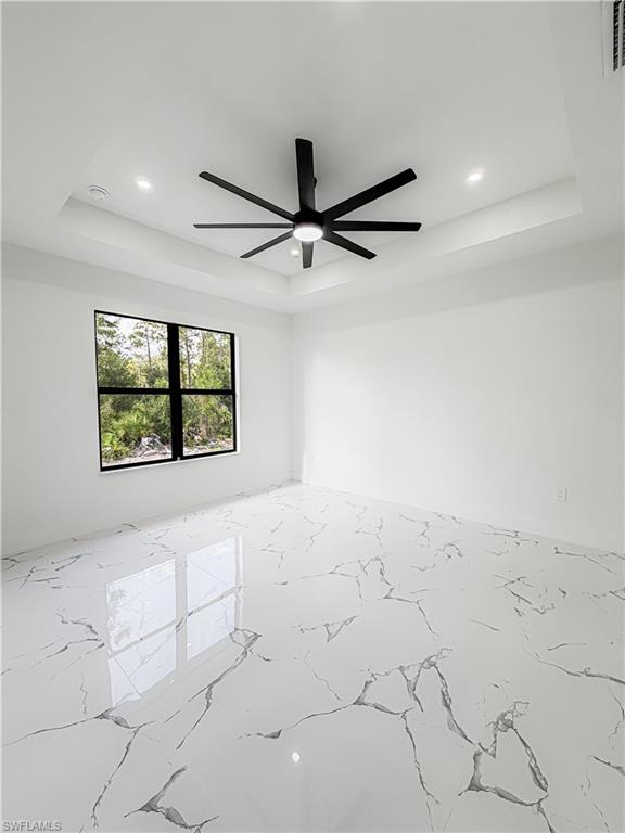 Spacious room featuring a tray ceiling with recessed lighting, a modern black ceiling fan, and large format polished tile flooring