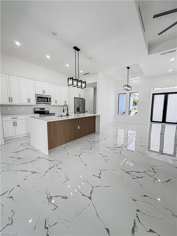Open-concept interior featuring large format marble-look tile flooring, a kitchen island with a slatted wood-finish base, white shaker cabinetry, stainless steel appliances, and contemporary pendant lighting