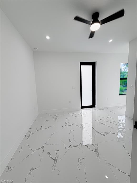 Spacious room featuring large format tile flooring with distinctive veining, a modern ceiling fan with integrated lighting, recessed lighting, and a contemporary door with a frosted glass panel