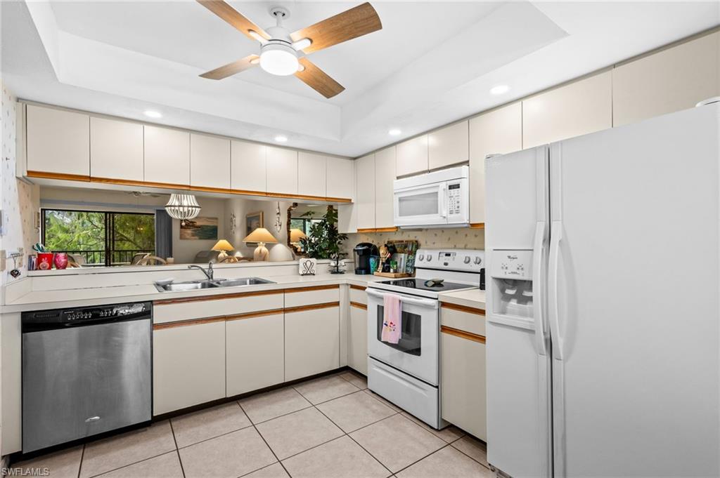 U-shaped kitchen featuring wood-finish cabinetry, tile flooring, and integrated white appliances