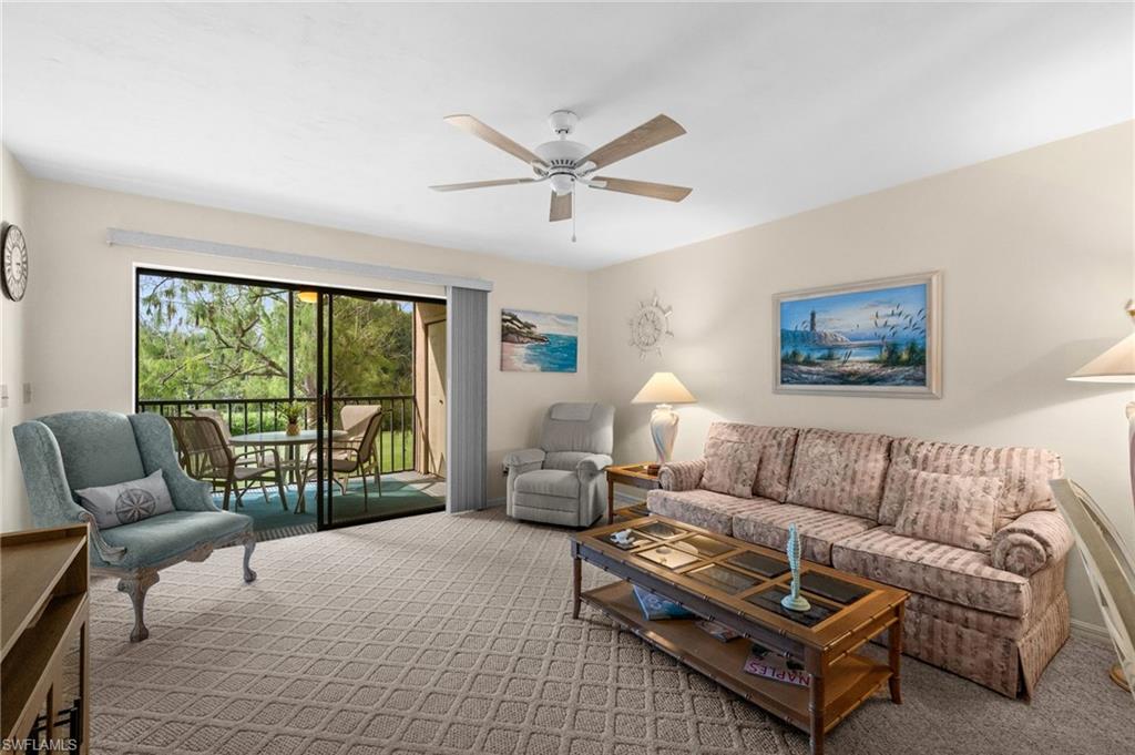 Living area with patterned carpet, a ceiling fan, and sliding glass doors opening to a screened balcony