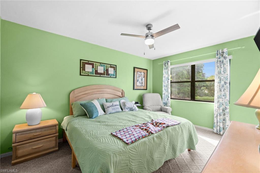 Bedroom featuring a light green wall color, a window with outdoor tree scenery, a ceiling fan with integrated lighting, and neutral-toned carpeting