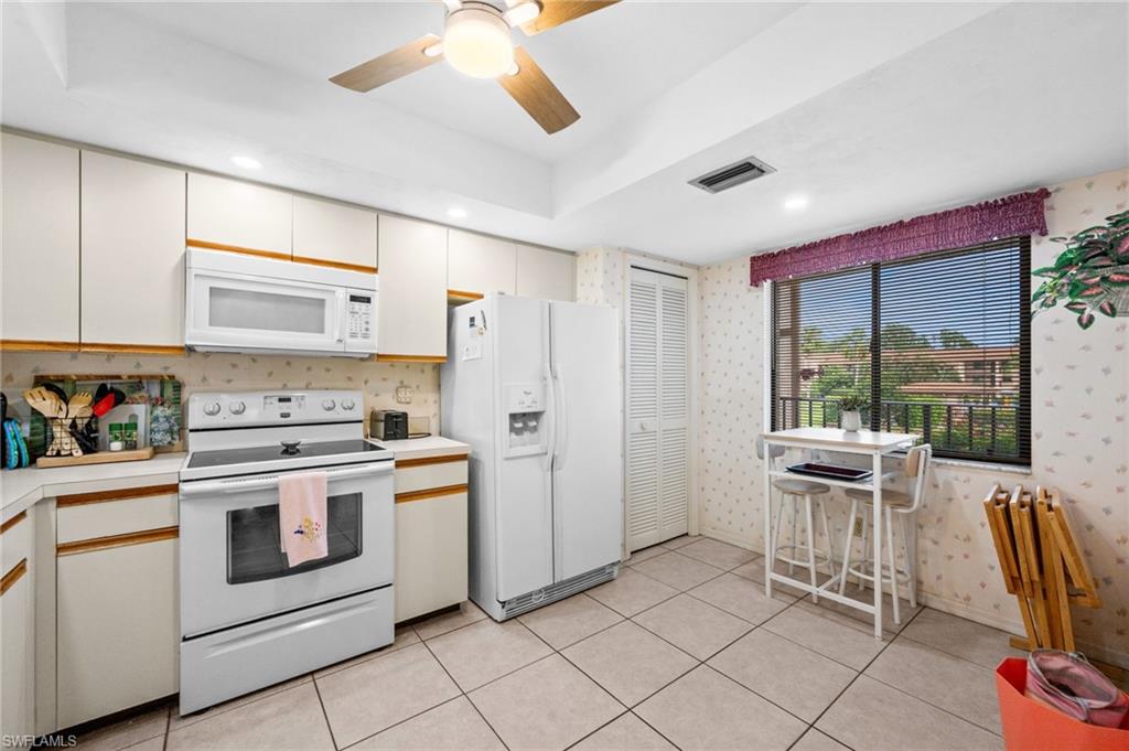 Kitchen featuring white cabinetry, white appliance suite, recessed lighting, ceiling fan, and large window with exterior view