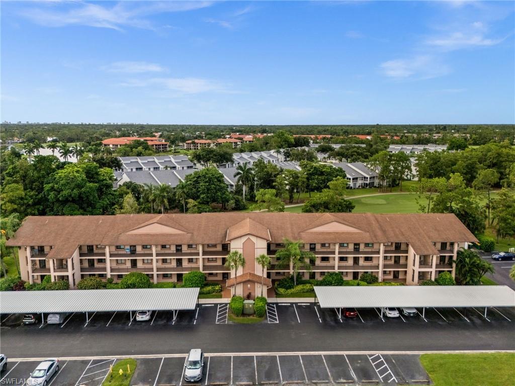 Multi-story residential building featuring balconies, covered parking, and an expansive paved lot