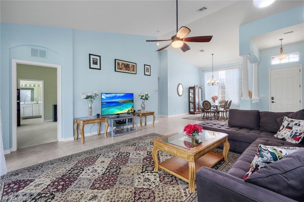 Spacious living area featuring high vaulted ceilings, light tile flooring, an arched doorway, and a ceiling fan