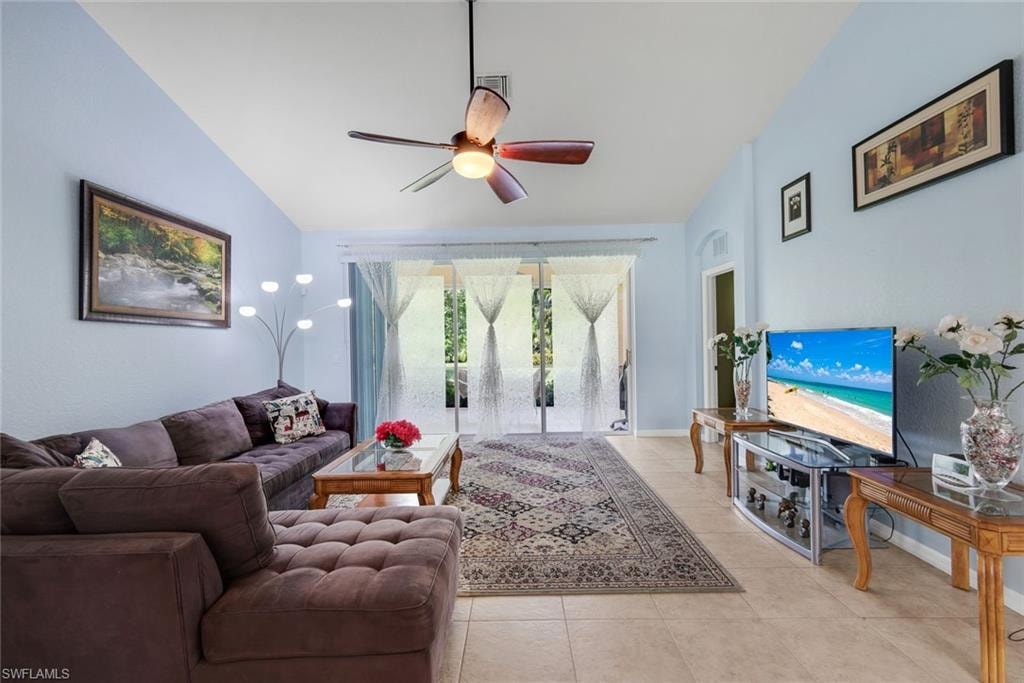 Spacious living area featuring tile flooring, vaulted ceilings, a ceiling fan with integrated lighting, and sliding glass doors providing abundant natural light