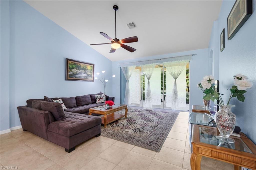 Spacious living area featuring vaulted ceilings, a ceiling fan, light blue wall finishes, and tile flooring