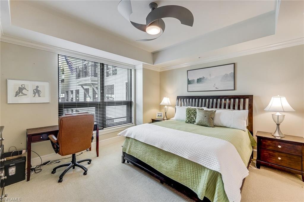 Spacious sleeping area featuring a tray ceiling with a modern ceiling fan, crown molding, and large windows with horizontal blinds