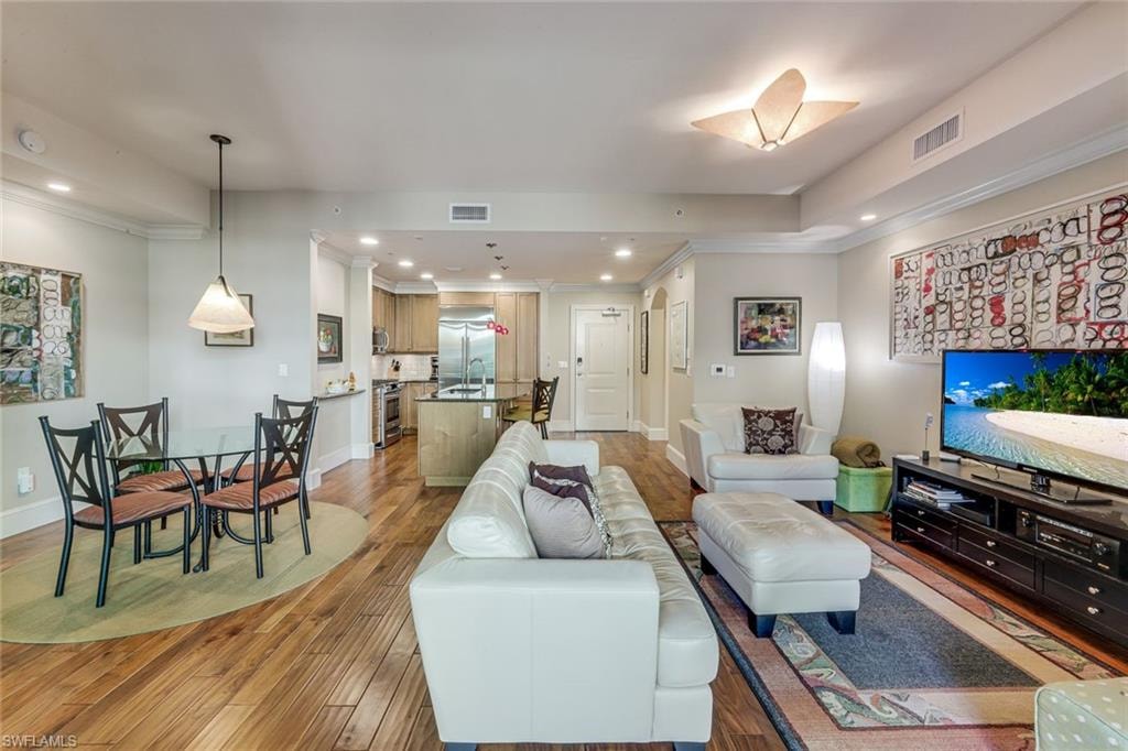 Open-concept living space featuring wood-finish flooring, recessed lighting, and crown molding