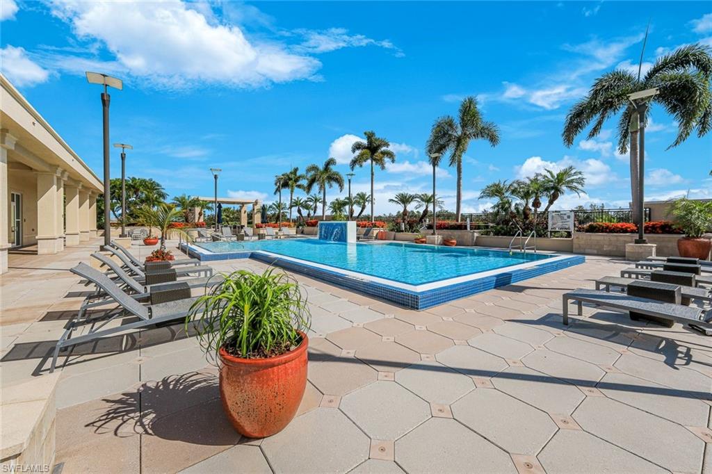 Resort-style pool area featuring a rectangular pool with blue tiled trim, surrounding paver patio, a built-in water feature, and mature palm trees